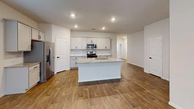 a large kitchen with kitchen island a sink dishwasher a refrigerator and white cabinets with wooden floor