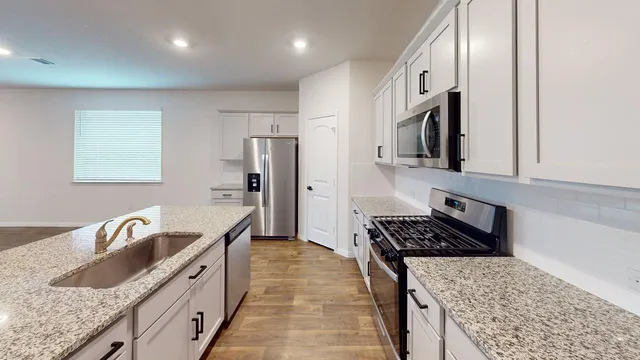 a kitchen with granite countertop a stove a sink and a refrigerator