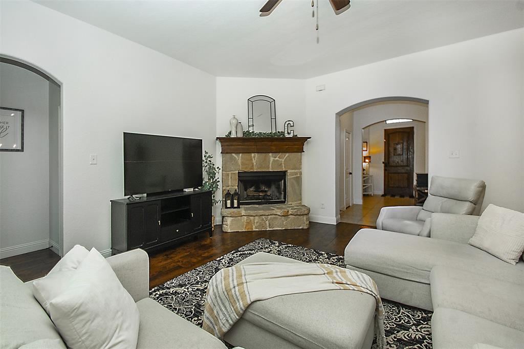 5809 Yellow Rose Court Midlothian, TX 76065 - Photo 11 of 33 Living area featuring a stone-clad fireplace with a wood mantel, rich wood-finish flooring, and arched doorways