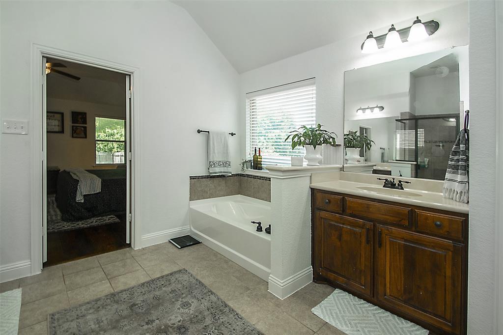 5809 Yellow Rose Court Midlothian, TX 76065 - Photo 15 of 33 Bathroom featuring a built-in tub with tile surround, a single vanity with wood cabinetry and light-toned countertop, a large mirror, and tile flooring