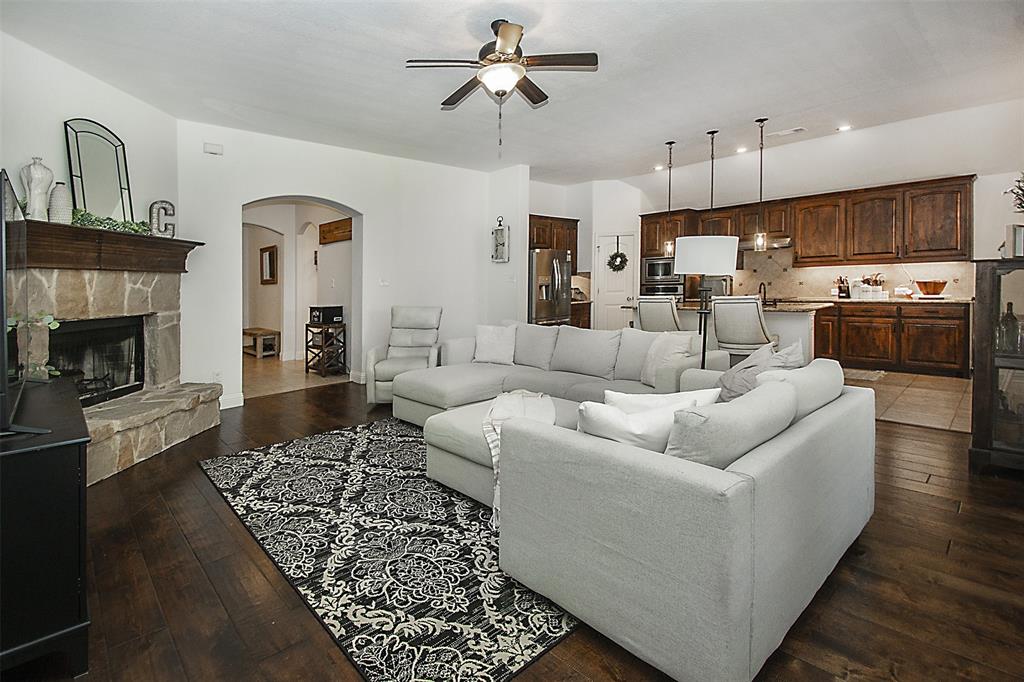 5809 Yellow Rose Court Midlothian, TX 76065 - Photo 4 of 33 Open-concept living space featuring wood-finish flooring, a stone fireplace with a wood mantle, and an arched entryway