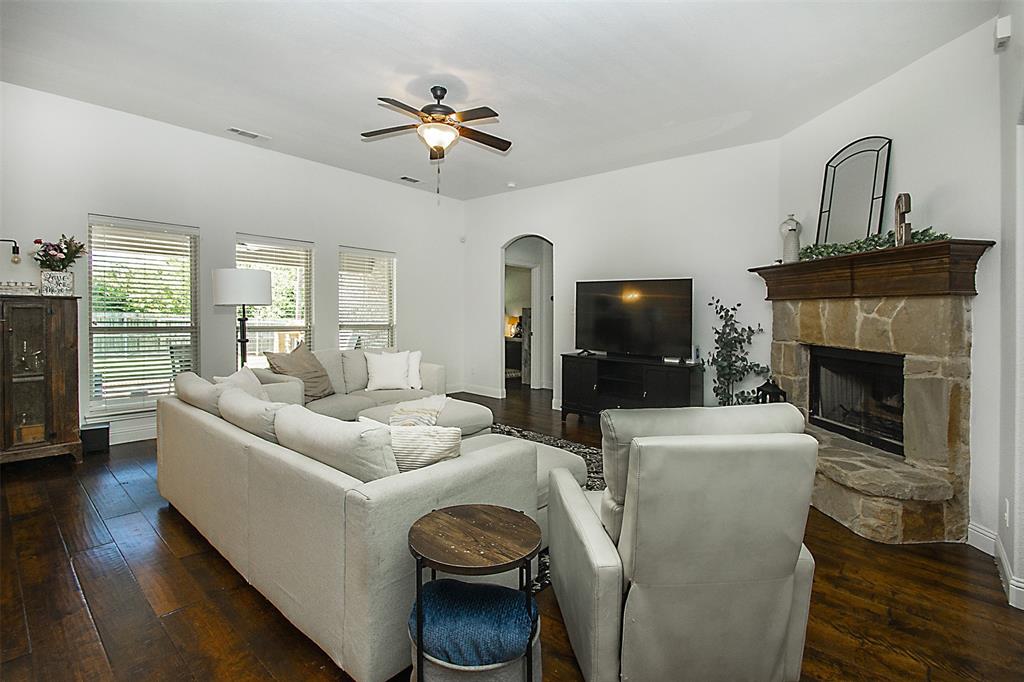 5809 Yellow Rose Court Midlothian, TX 76065 - Photo 6 of 33 Living area featuring wood-finish flooring, a corner stone-faced fireplace with a wood mantel, multiple windows with blinds, a ceiling fan with integrated lighting, and an arched doorway