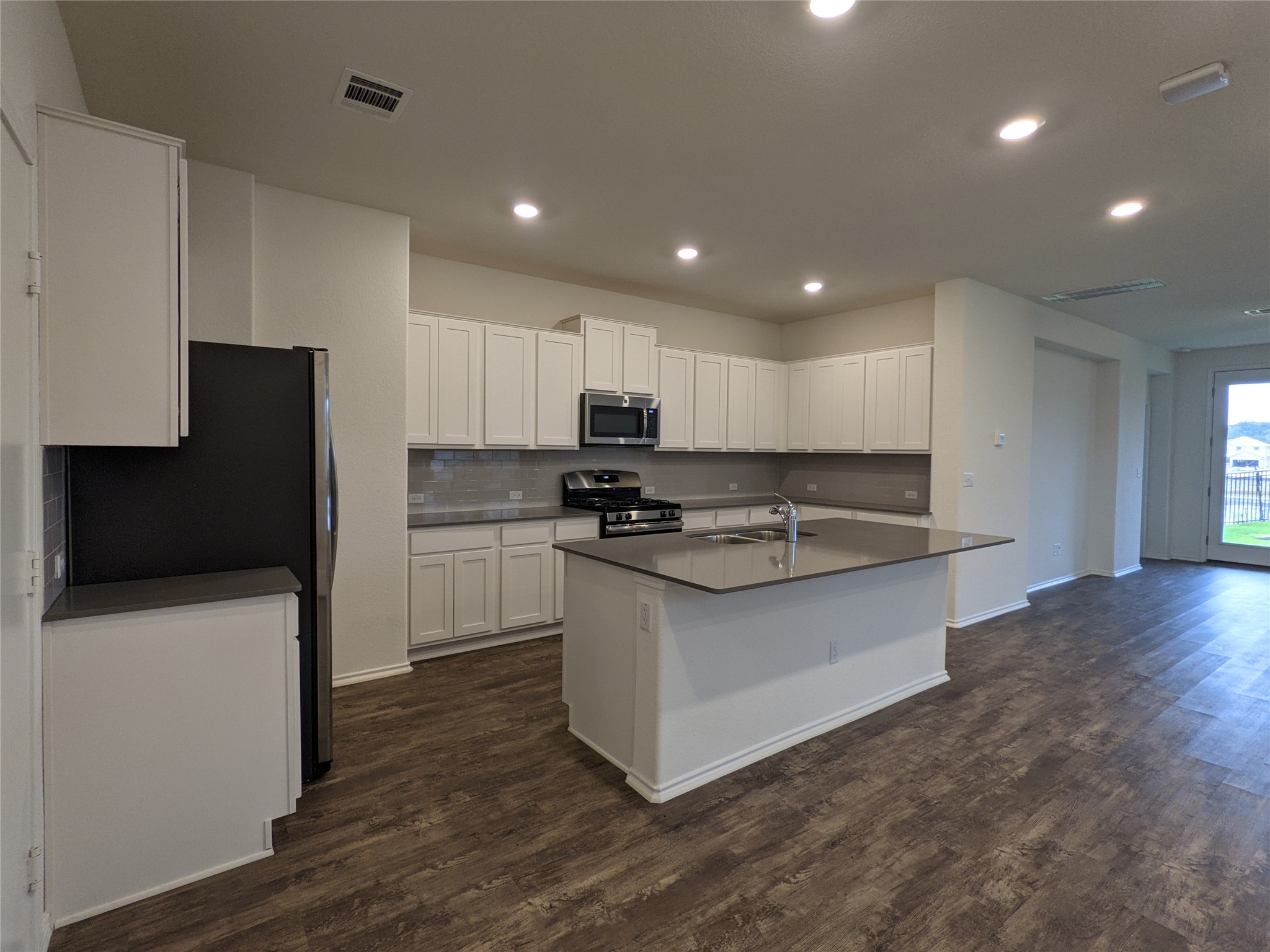 100 Montauk Loop Georgetown, TX 78628 - Photo 7 of 21 A well-lit culinary space showcases an island with a sink, white cabinetry, and durable wood-look flooring.