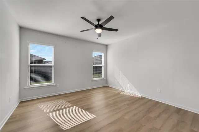 an empty room with wooden floor ceiling fan and windows