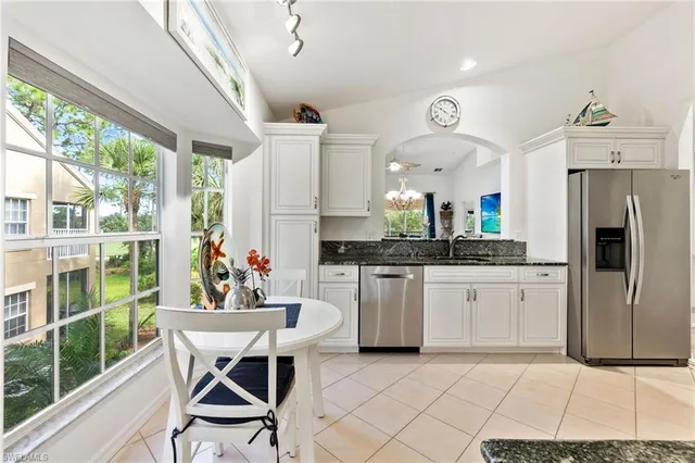 a kitchen with stainless steel appliances kitchen island granite countertop a refrigerator a sink dishwasher a dining table and chairs with wooden floor
