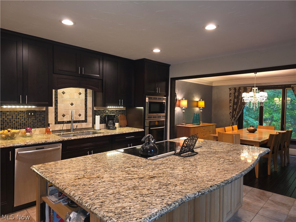 2868 Shade Road Akron, OH 44333 - Photo 11 of 49 Kitchen featuring a large central island with a built-in cooktop, dark wood cabinetry, stainless steel dishwasher, integrated wall oven and microwave, and a decorative tile backsplash above the sink