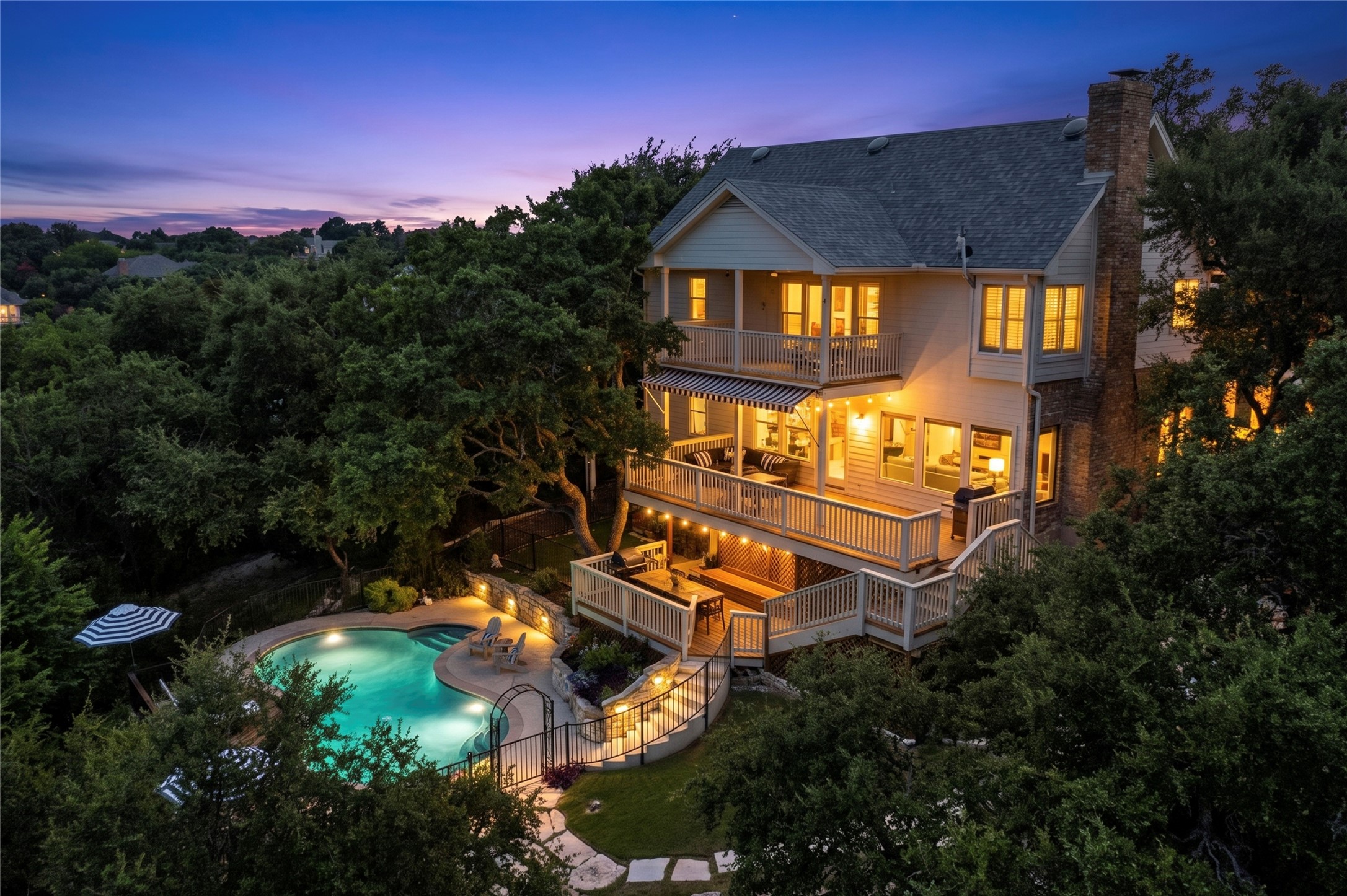 3107 Lookout Lane Austin, TX 78746 - Photo 39 of 39 Multilevel decks descend to a sparkling pool, embraced by lush trees under a vibrant twilight sky.