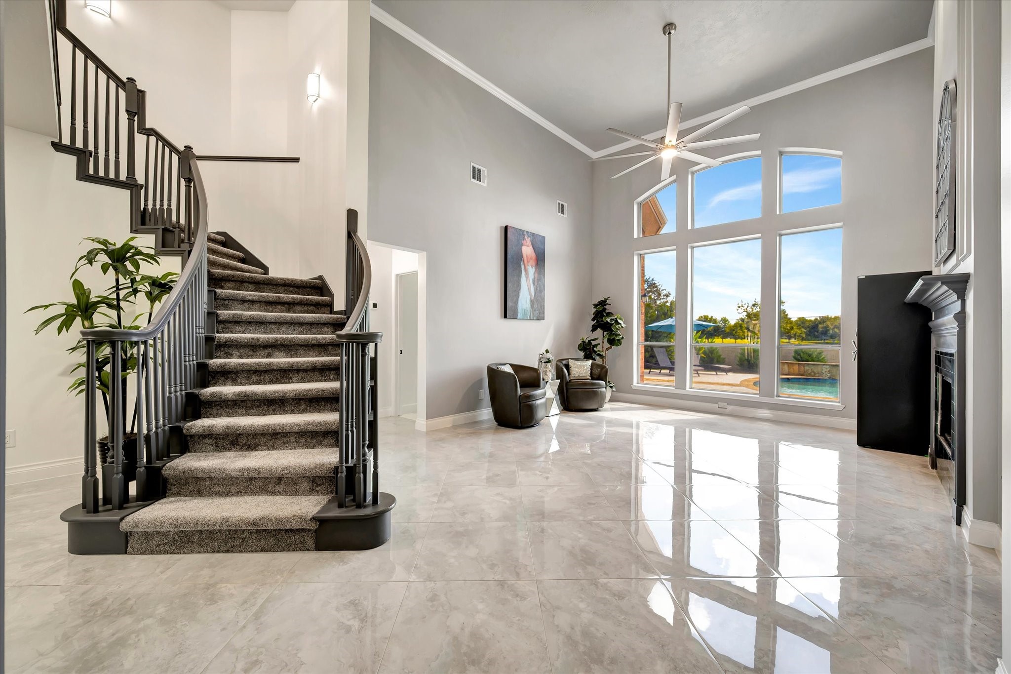 2847 Everett Drive Friendswood, TX 77546 - Photo 14 of 50 This photo showcases a spacious, modern living area with high ceilings and large windows offering plenty of natural light. The room features a sleek staircase, glossy tiled floors, and a contemporary ceiling fan. A view of the outdoor pool area is visible, enhancing the home's appeal.