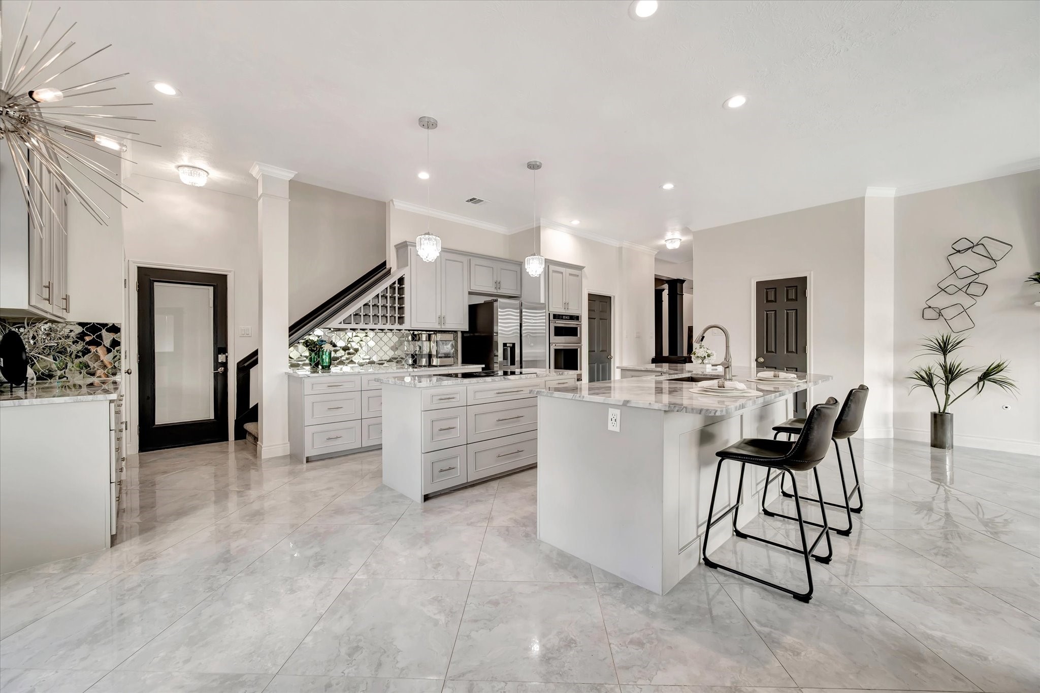2847 Everett Drive Friendswood, TX 77546 - Photo 21 of 50 This photo showcases a spacious, modern kitchen with sleek gray cabinetry, marble countertops, and a large island with seating. The open layout features elegant tile flooring, contemporary lighting, and stainless steel appliances, creating a stylish and functional space.
