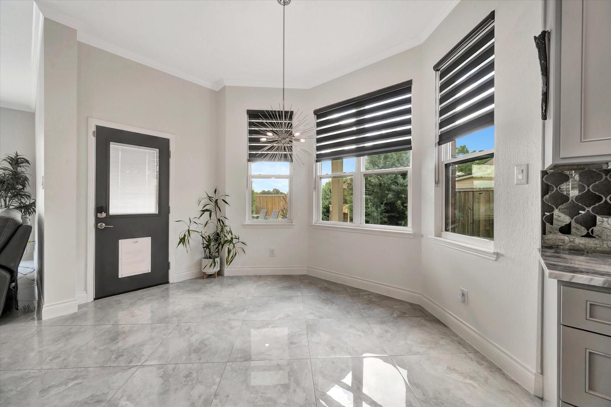 2847 Everett Drive Friendswood, TX 77546 - Photo 23 of 50 This photo showcases a bright, modern breakfast area with large windows, stylish blinds, and glossy tile floors. The space features a contemporary light fixture, a sleek black door with a pet flap, and a view of the outdoors.