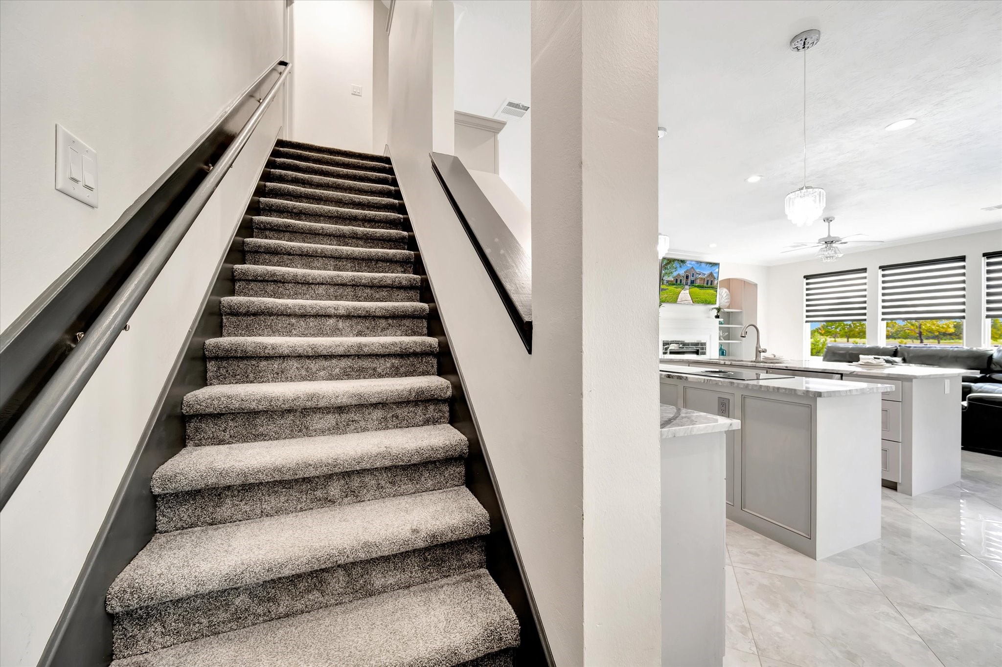 2847 Everett Drive Friendswood, TX 77546 - Photo 26 of 50 Modern home interior featuring a carpeted staircase leading upstairs. The open-concept kitchen and living area to the right are bright and spacious, with marble countertops, sleek cabinetry, and large windows allowing plenty of natural light.