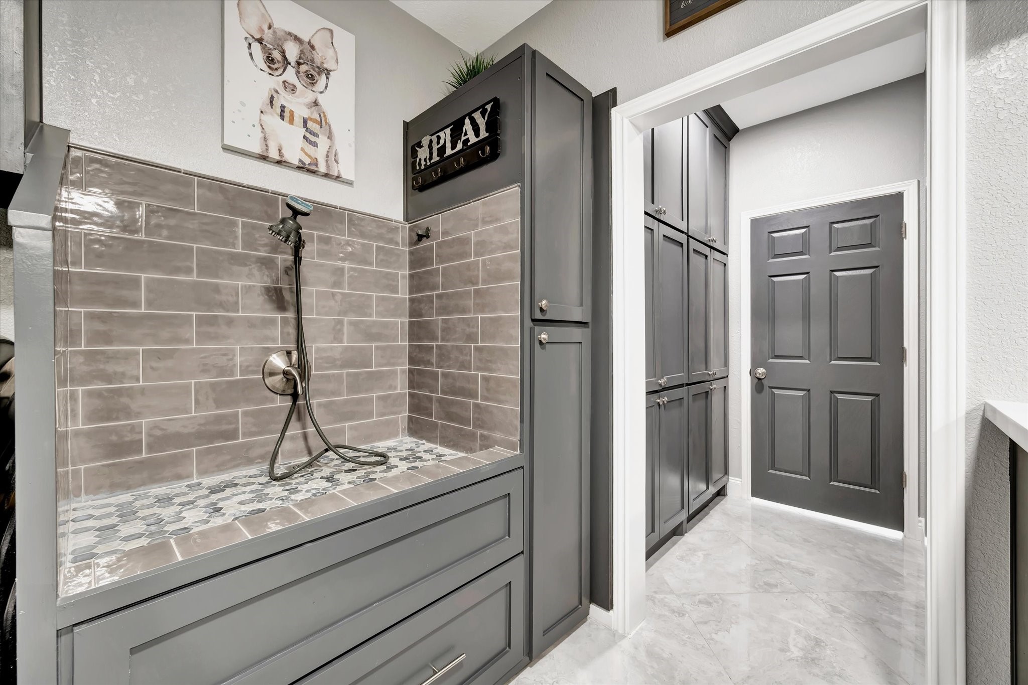 2847 Everett Drive Friendswood, TX 77546 - Photo 31 of 50 This photo showcases a dog washing station, featuring gray subway tiles and a handheld shower. Ample storage is provided by sleek cabinets for a clean, modern look.