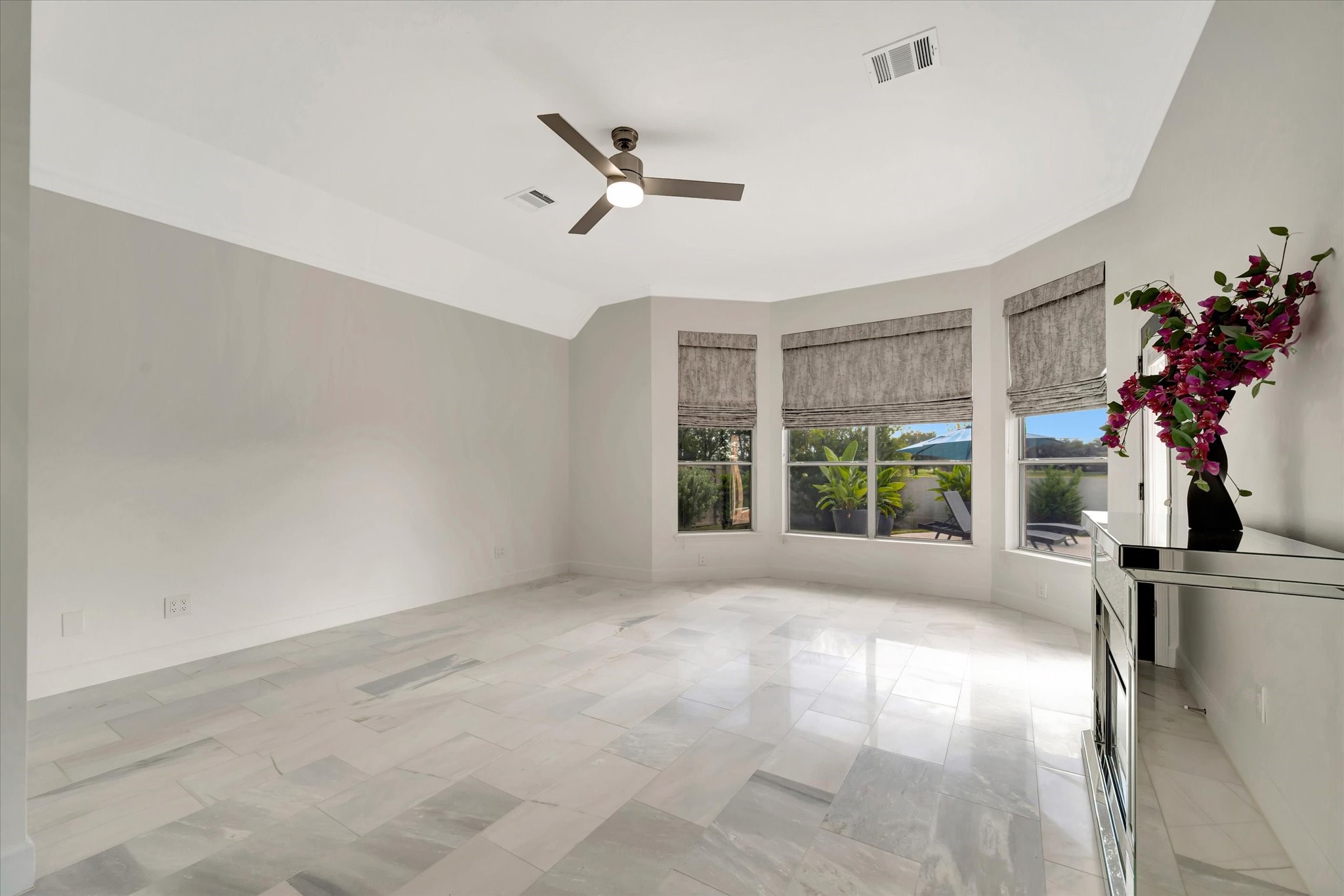 2847 Everett Drive Friendswood, TX 77546 - Photo 32 of 50 This bright Primary bedroom features large windows with shades, a ceiling fan, and sleek marble flooring. It offers a clean, modern aesthetic with neutral tones and a view of greenery outside with room for a sitting area.