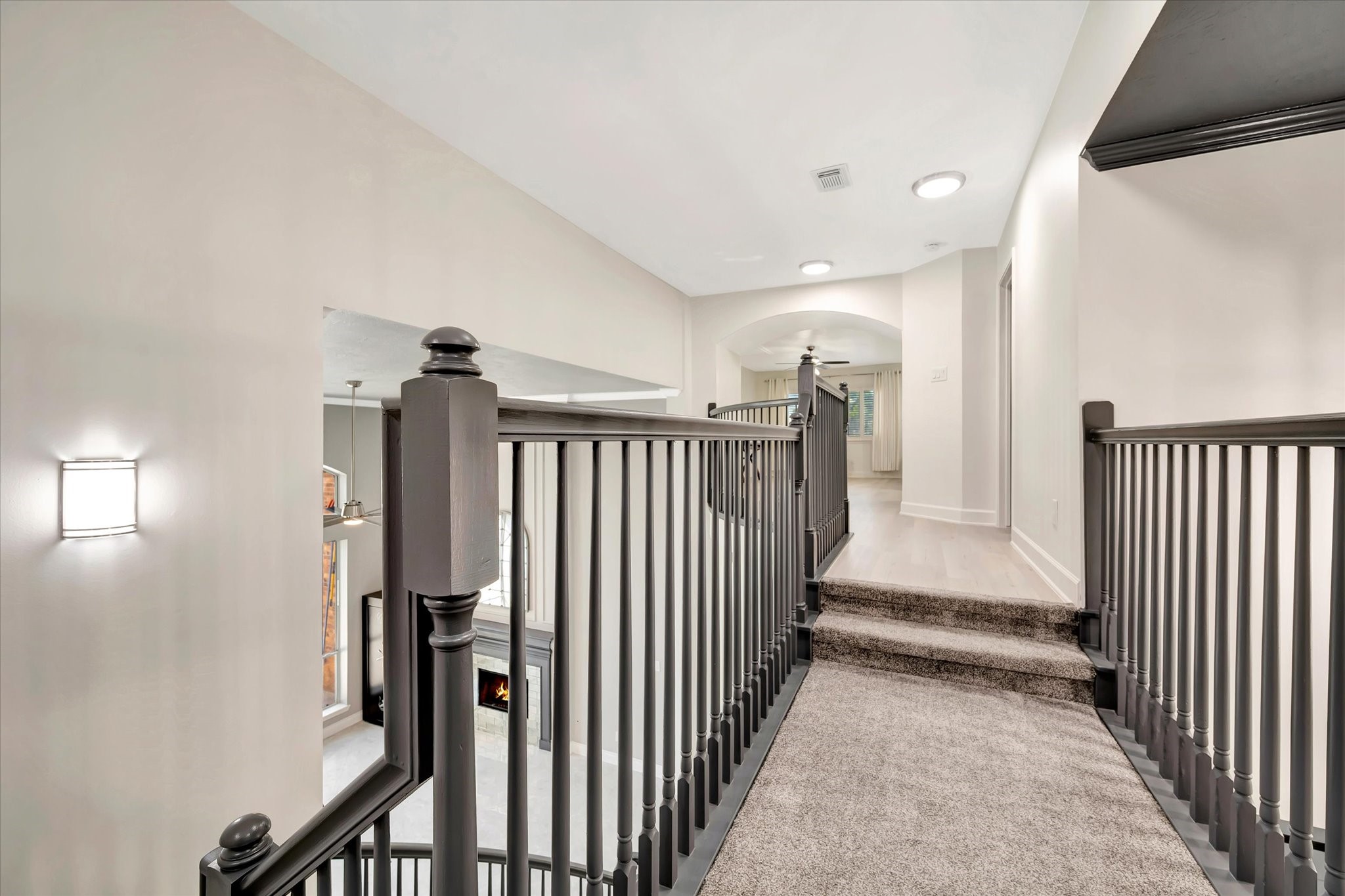 2847 Everett Drive Friendswood, TX 77546 - Photo 40 of 50 This photo showcases a modern, open hallway with a stylish railing overlooking a lower living area with a fireplace. The space has neutral walls, carpeted stairs, and ample natural light, creating a bright and welcoming atmosphere.