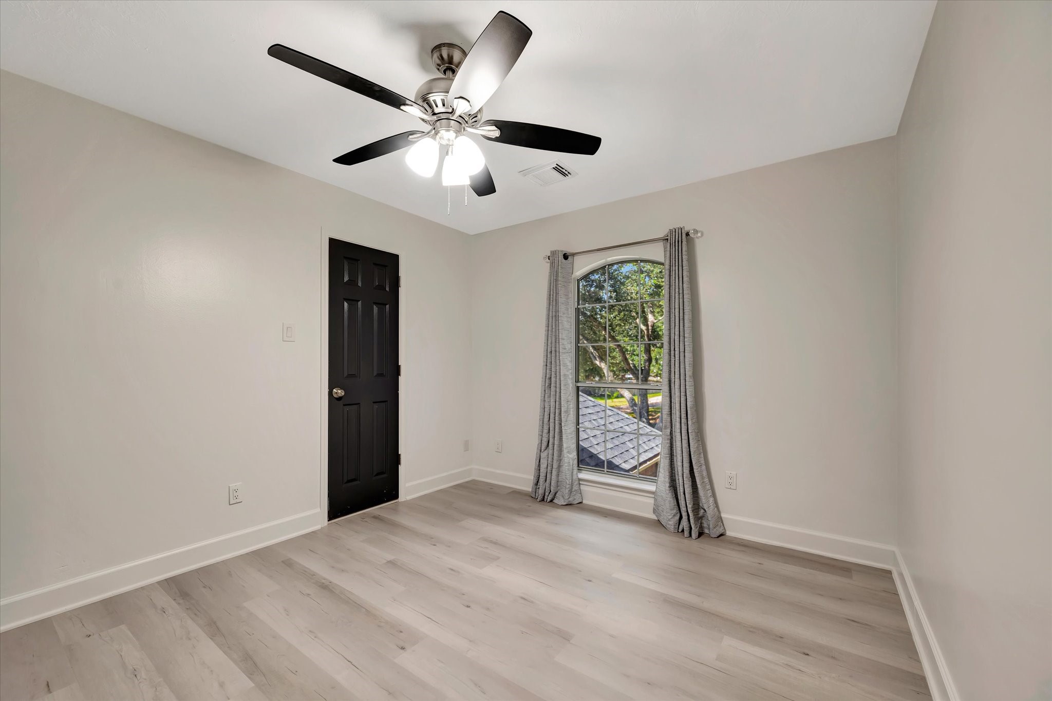 2847 Everett Drive Friendswood, TX 77546 - Photo 41 of 50 This room features a neutral color palette with light wood flooring, a ceiling fan, and a large window with curtains providing natural light. The black door adds a modern touch. Ideal secondary bedroom