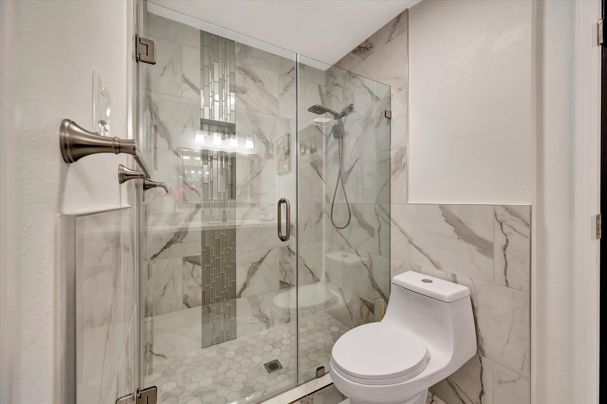 2847 Everett Drive Friendswood, TX 77546 - Photo 43 of 50 This modern bathroom features a sleek glass-enclosed shower with stylish tile accents and a contemporary commode. The space is bright and elegantly designed with marble-like wall tiles, offering a clean and sophisticated look.