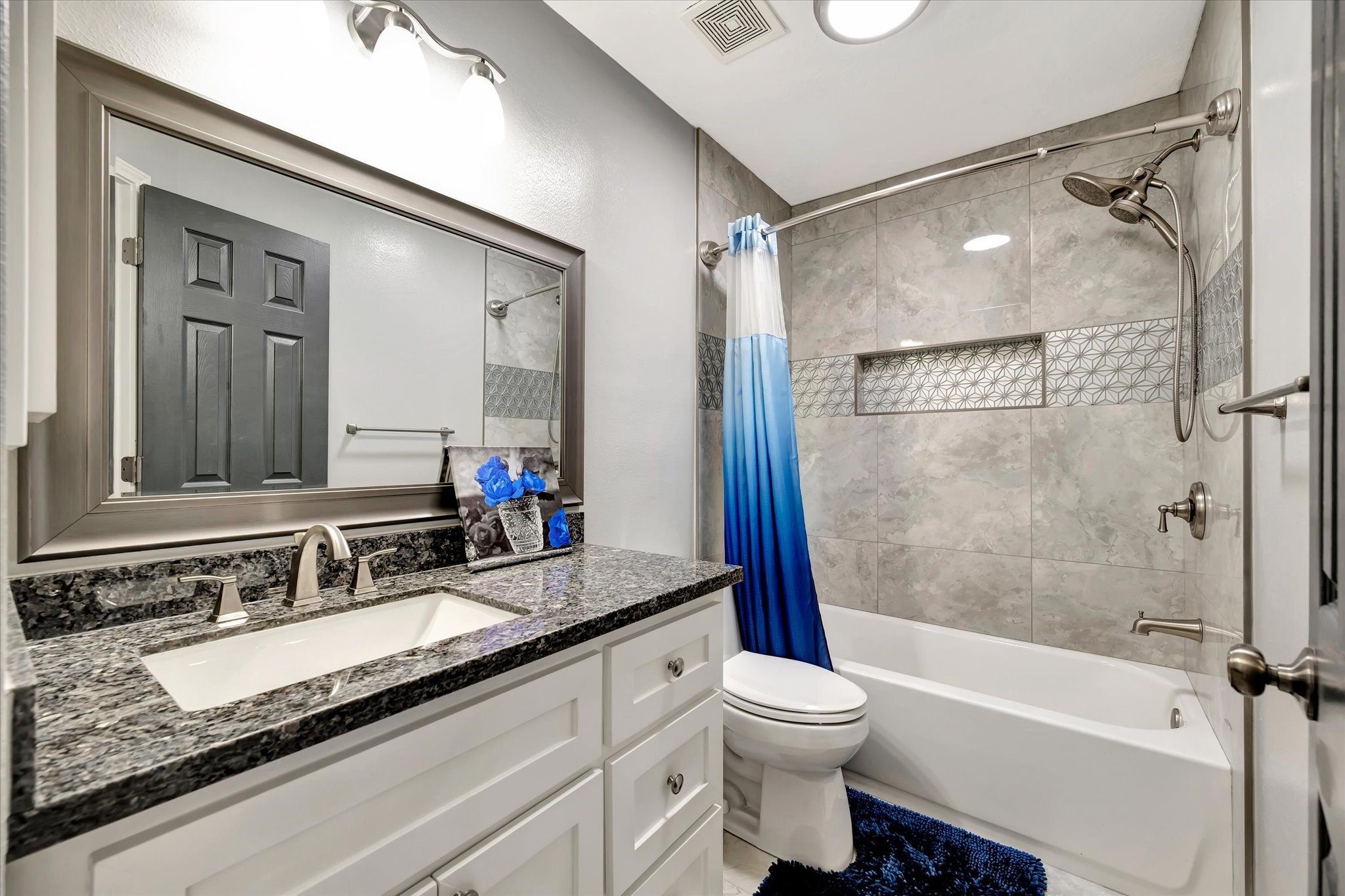 2847 Everett Drive Friendswood, TX 77546 - Photo 45 of 50 Modern bathroom featuring a granite countertop with a sleek sink, stylish fixtures, and a large framed mirror. The shower-tub combo has elegant gray tile with decorative accents. The space is well-lit with contemporary lighting.