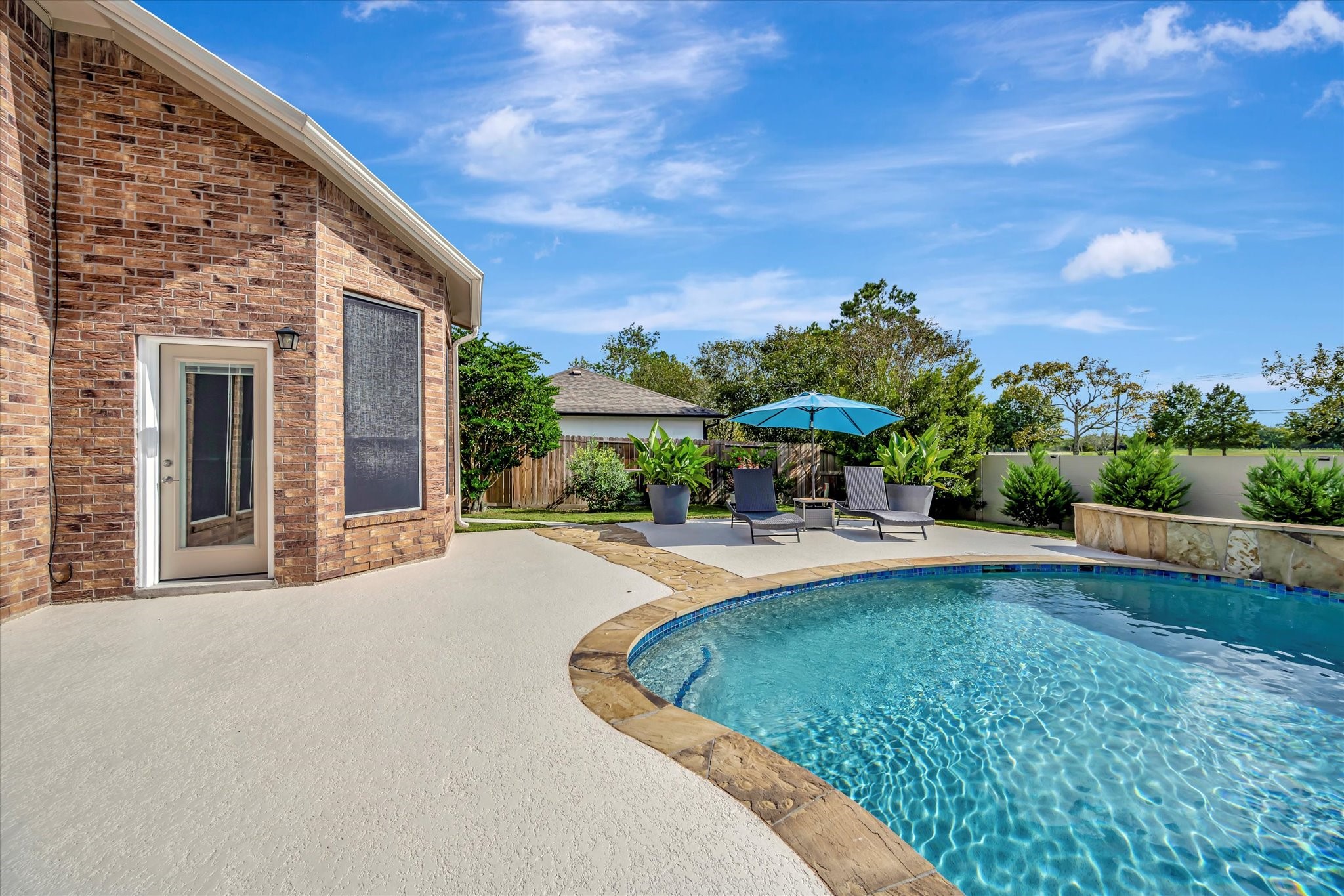 2847 Everett Drive Friendswood, TX 77546 - Photo 6 of 50 This photo showcases a spacious backyard featuring a sparkling pool with a stone edge, surrounded by greenery.