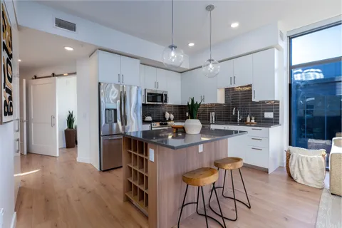 a kitchen with stainless steel appliances kitchen island granite countertop a refrigerator a stove top oven a sink dishwasher and white cabinets with wooden floor