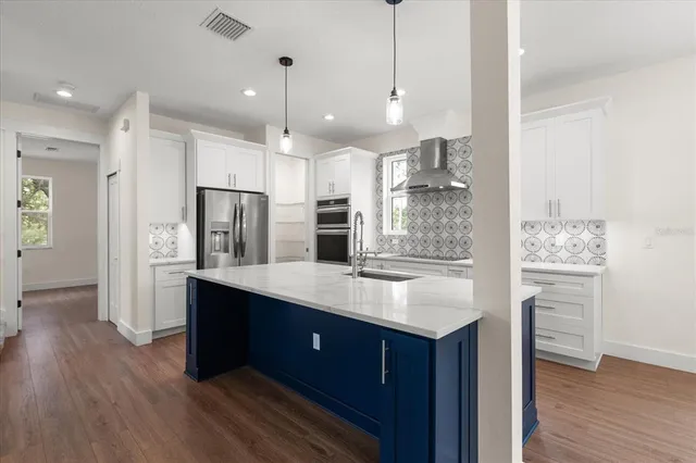 a kitchen with stainless steel appliances kitchen island granite countertop a refrigerator a sink dishwasher a oven and white cabinets with wooden floor