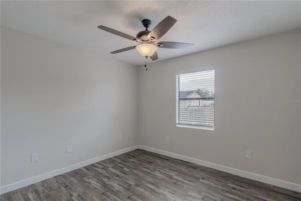 an empty room with wooden floor fan and windows