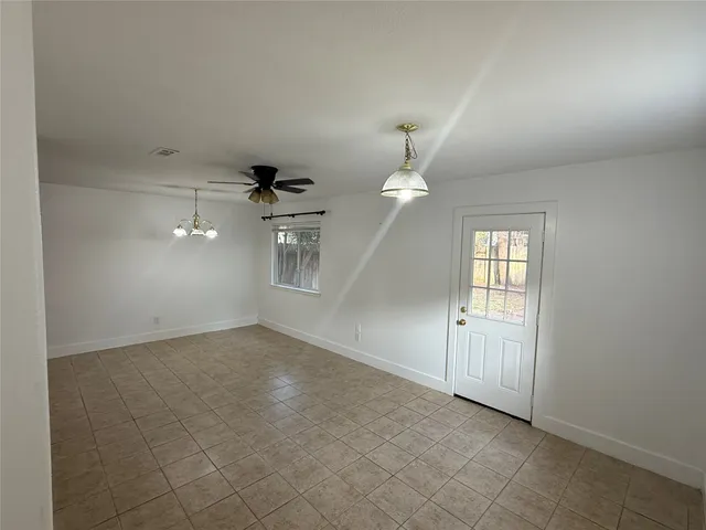an empty room with chandelier fan and windows