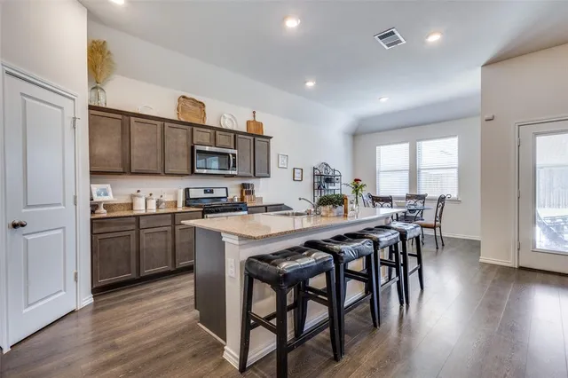 a kitchen with stainless steel appliances granite countertop wooden floor a dining table and chairs