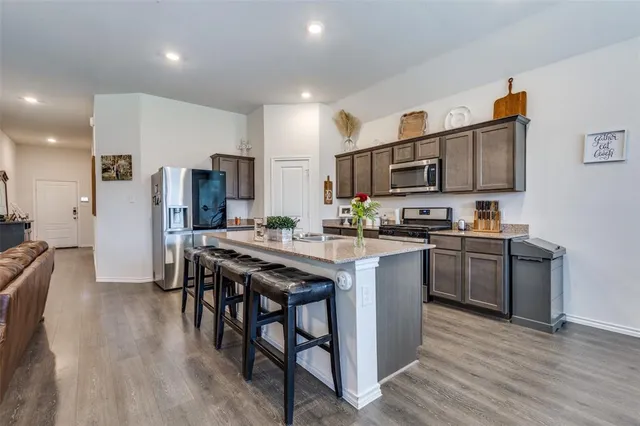 a kitchen with stainless steel appliances granite countertop a refrigerator a stove top oven a sink dishwasher and white cabinets with wooden floor