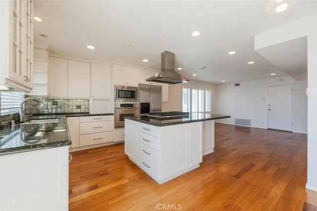 a large kitchen with stainless steel appliances granite countertop a stove a sink a refrigerator and white cabinets with wooden floor