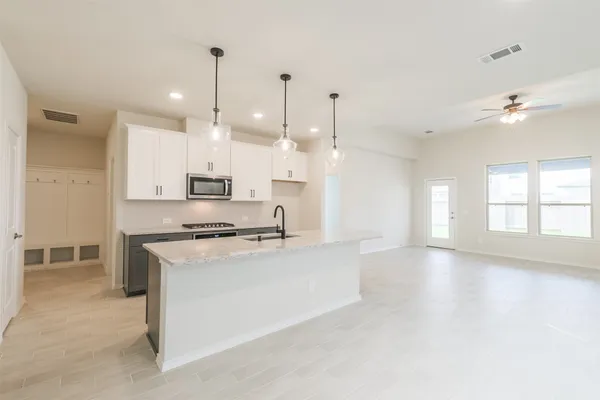 a large kitchen with stainless steel appliances granite countertop a stove a sink a refrigerator white cabinets and couches with wooden floor