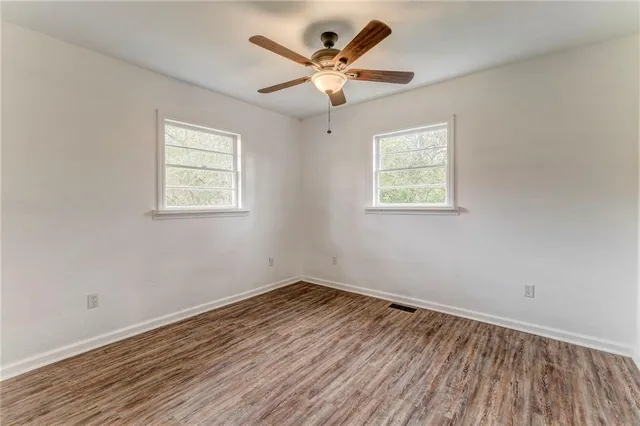 an empty room with wooden floor chandelier fan and windows