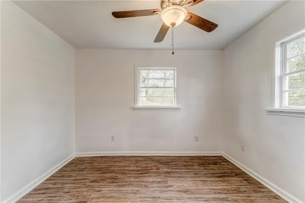 an empty room with wooden floor chandelier fan and windows