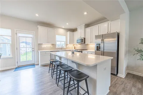 a kitchen with stainless steel appliances granite countertop a refrigerator a sink a stove a dining table and chairs