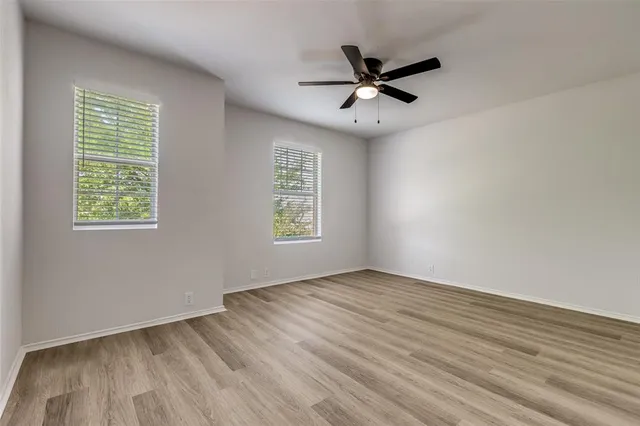 an empty room with wooden floor fan and windows