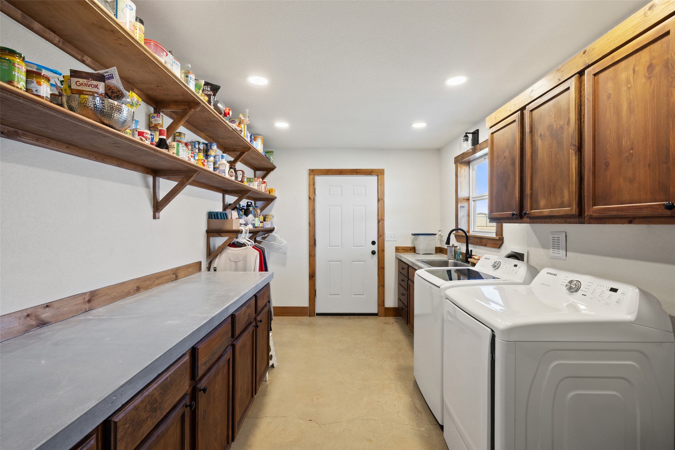 664 Martindale Falls Road Martindale, TX 78655 - Photo 12 of 21 Utility room featuring extensive built-in shelving, concrete-finish countertops, wood-finish cabinetry, a utility sink with a matte black faucet, and overhead recessed lighting