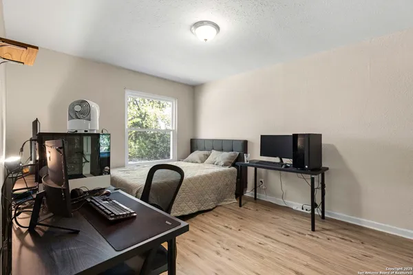 a bedroom with a bed a computer on a desk and chair with wooden floor