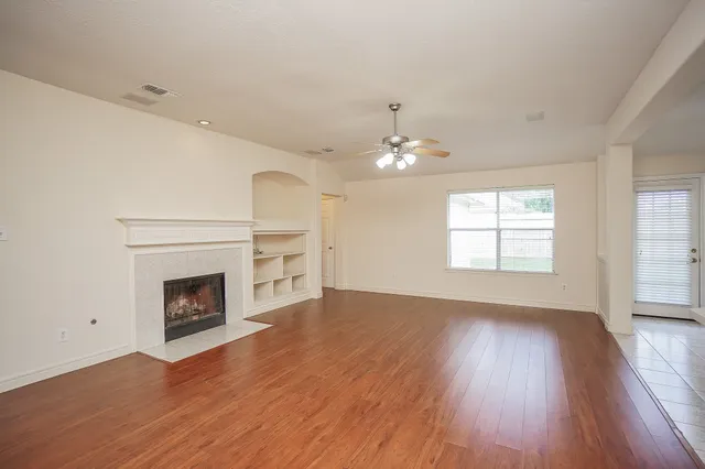 an empty room with wooden floor fireplace and windows