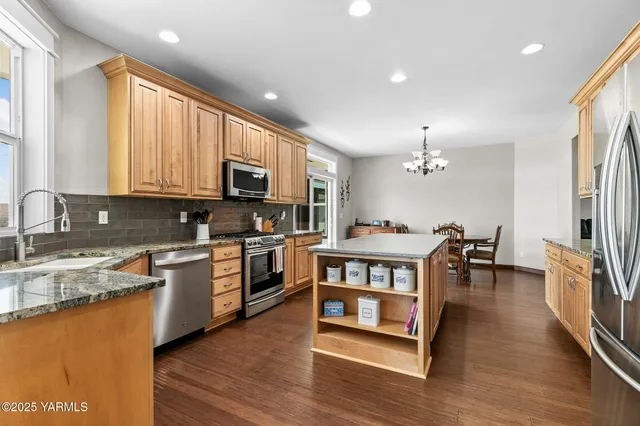 a kitchen with stainless steel appliances granite countertop a stove top oven a sink dishwasher a dining table and chairs with wooden floor