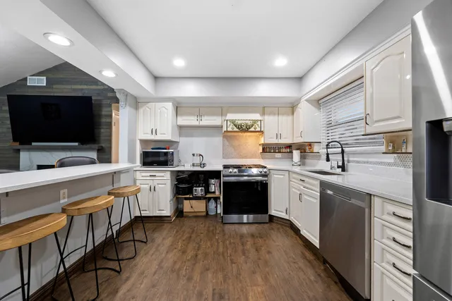 a kitchen with stainless steel appliances a sink dishwasher a refrigerator a stove top oven a sink and dishwasher with wooden floor