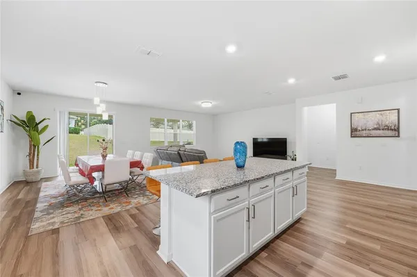 a open kitchen with stainless steel appliances granite countertop a stove top oven a sink dishwasher a dining table and chairs with wooden floor