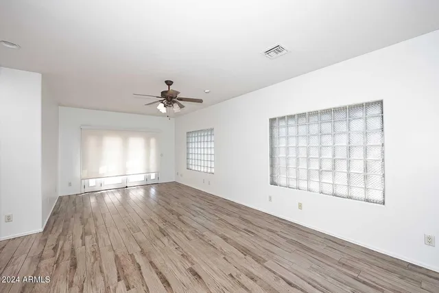 an empty room with wooden floor chandelier fan and windows