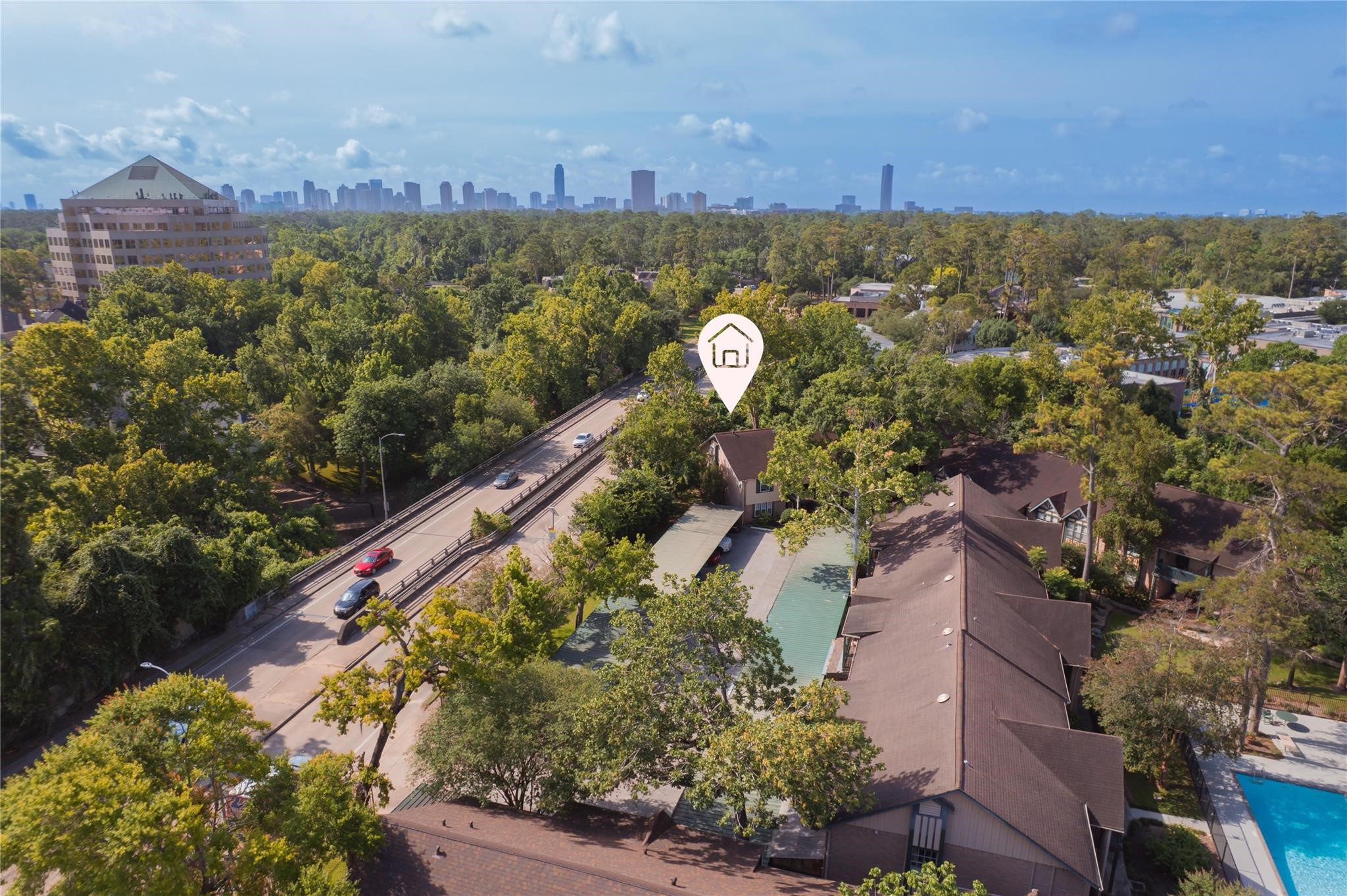 8223 Kingsbrook Road, Unit 212 Houston, TX 77024 - Photo 10 of 10 This aerial photo showcases a property nestled among lush trees, offering a serene environment. It’s conveniently located near a main road and features proximity to urban amenities, with a view of the city skyline in the distance.