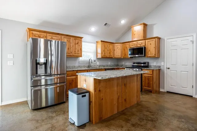 a kitchen with kitchen island a counter top space cabinets stainless steel appliances and a window