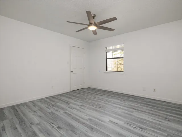 an empty room with wooden floor window and ceiling fan
