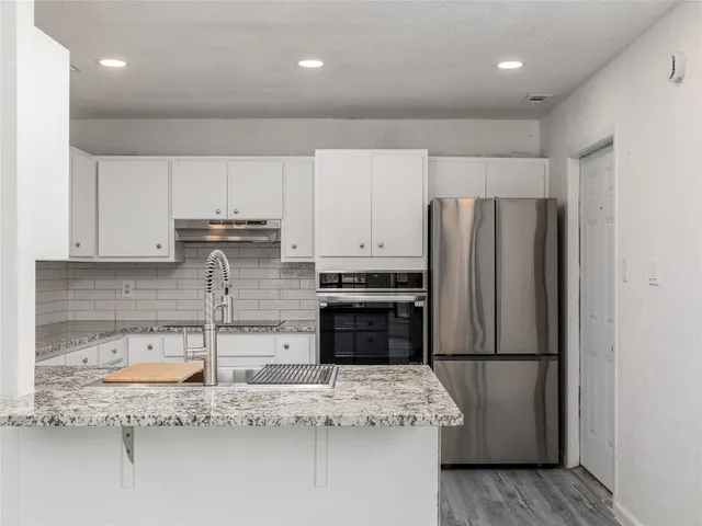 a kitchen with kitchen island granite countertop a refrigerator oven a sink and white cabinets