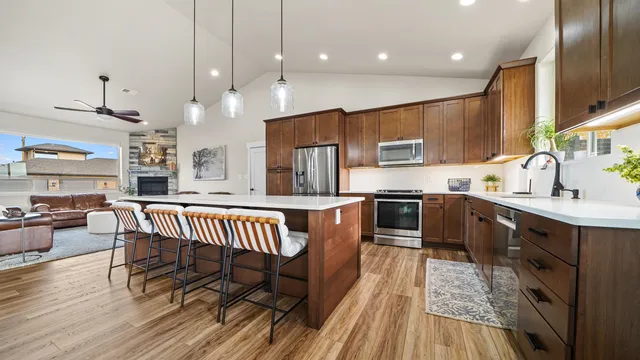 a kitchen with stainless steel appliances granite countertop a refrigerator a sink dishwasher a stove and a dining table with wooden floor