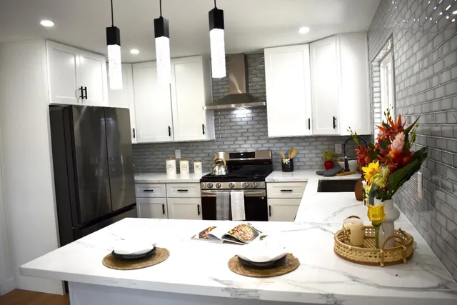 a kitchen with stainless steel appliances kitchen island granite countertop a refrigerator a stove a sink and white cabinets with wooden floor