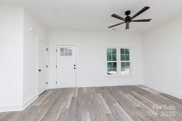 an empty room with wooden floor a ceiling fan and windows