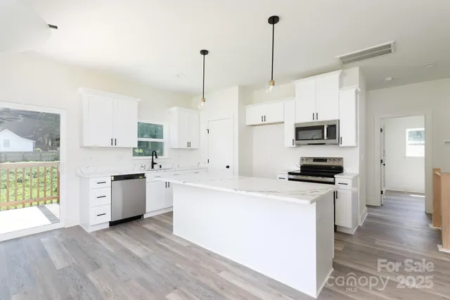 a kitchen with stainless steel appliances white cabinets a sink a stove a refrigerator and a window