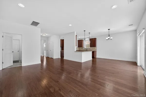 a view of an empty room with wooden floor and a kitchen
